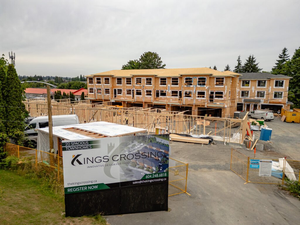 "Construction site of Kings Crossing townhomes in Abbotsford, with wooden framing and partially built units visible, and a promotional sign in the foreground."